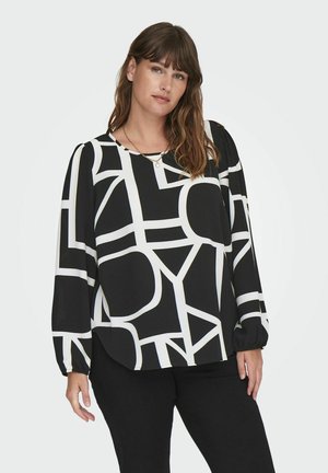 Blouse noire à manches longues avec de grands motifs géométriques blancs, décolleté arrondi et poignets élastiqués. Texture de tissu douce, coupe décontractée.