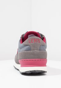Graue und rosa Sneaker mit einem Obermaterial aus Wildleder und Textil, ausgestattet mit einem gepolsterten Schaft, einer weißen Zwischensohle und einer Gummisohle für besseren Halt.