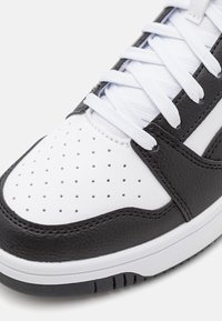 Gros plan sur l'avant d'une basket noire et blanche avec cuir blanc perforé, surpiqûres en cuir noir et lacets blancs sur une semelle blanche.