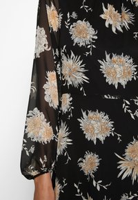 Blommig svart klänning med genomskinliga långa ärmar, broderade vita och orange blommor, samt en figurnära bodice med subtila rynkor.