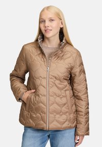 Beżowa pikowana kurtka z wzorem w kształcie serca, zamek błyskawiczny, wysoki kołnierz i podszewka w panterkę. Posiada boczne kieszenie i długie rękawy.