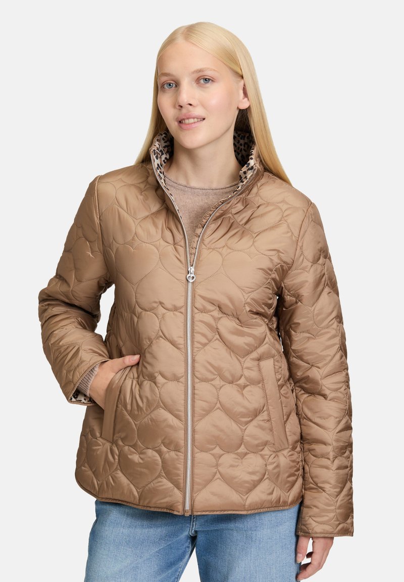 Beżowa pikowana kurtka z wzorem w kształcie serca, zamek błyskawiczny, wysoki kołnierz i podszewka w panterkę. Posiada boczne kieszenie i długie rękawy.