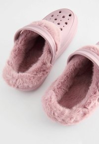 Roze schoeisel met een zachte imitatiebont voering, ronde vorm, ventilerende gaten bovenop en een stevige band over de middenvoet.