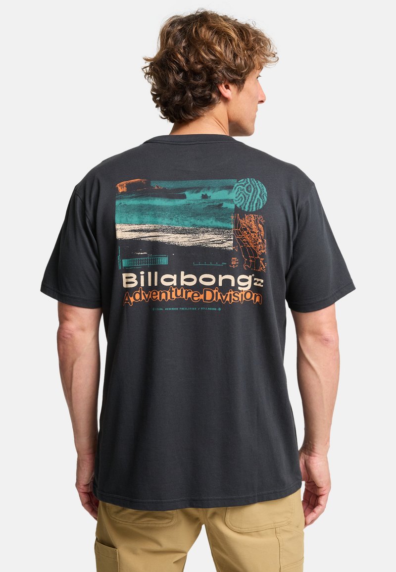 Musta puuvillapaita, jossa on värikäs graafinenPRINTTI selässä. Teksti "Billabong Adventure Division" ja abstraktit kuviot.