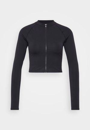 Czarny, krótki top z długim rękawem i wysokim kołnierzem, z zamkiem błyskawicznym z przodu i gładką teksturą. Posiada rękawy raglanowe dla swobody ruchów.