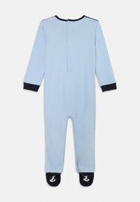 Light blue long-sleeve onesie with a button placket, navy cuffs, and matching footed bottom featuring a logo on the soles. Soft fabric texture.