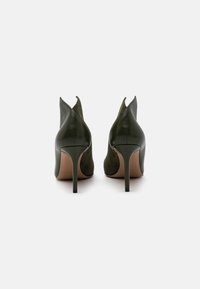 Zapatos de tacón de cuero y ante verde con punta afilada y diseño recortado en la parte trasera, que cuentan con un tacón de aguja delgada.