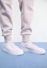 Světle fialové tenisky Nike Air Force 1 s bílými akcenty, s hladkým koženým povrchem, šněrováním a perforovanou špičkou.