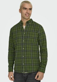 Zielona koszula zapinana na guziki w kratę, wykonana z miękkiego materiału, z kieszonką na piersi, w czarno-białą kratkę oraz tradycyjnym kroju kołnierzyka.