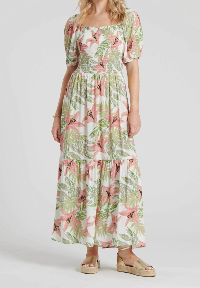 Femme portant une robe maxi blanche avec un imprimé floral tropical vert et rose, des manches bouffantes et des sandales compensées espadrilles.