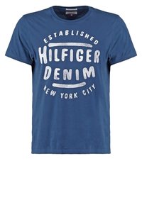 Modré bavlněné tričko s kulatým výstřihem, krátkými rukávy a výrazným bílým textem "HILFIGER DENIM" s uvedeným datem a místem vzniku.