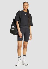 Svart kortärmad t-shirt och cykelbyxor med vitt Adidas-logotyp. Vita sneakers med svarta detaljer, iförd svarta och vita randiga strumpor. Stor tygväska.