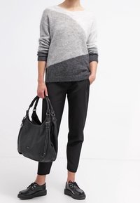 Persona che indossa un maglione grigio sfumato, pantaloni cropped neri, scarpe con platform nere e testurizzate, mentre tiene una grande borsa in pelle nera.