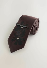 Silk tie in deep brown with a black floral print. Features a sleek, minimal black tie clip. Rolled presentation highlights the design's elegance.