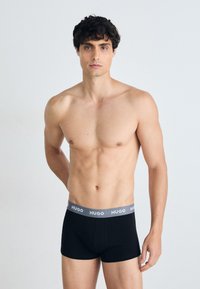 Boxer-briefs en coton noir avec une ceinture élastique grise arborant le logo "HUGO." Design simple sans motifs ni accents supplémentaires.