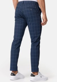 Marineblauwe geruite broek met een slim fit, zij- en achterzakken, en een knoopsluiting op de achterzak. Gecombineerd met witte sneakers.