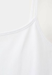 Gros plan d'un tissu blanc côtelé avec fines bretelles et bord cousu, montrant la texture et les détails du vêtement.