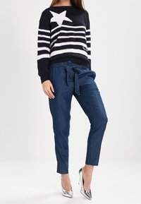Pull en maille rayé bleu marine et blanc avec une grande étoile blanche, associé à un pantalon bleu marine tapered et des escarpins argentés.