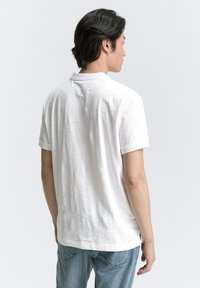 Weißes Kurzarm-T-Shirt aus strukturiertem Stoff, mit Rundhalsausschnitt und lockerer Passform, kombiniert mit hellblauen Jeans. Rückansicht.