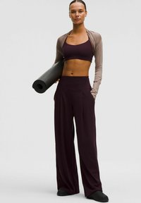 Urheiluasu, jossa on tumman viininpunainen lyhythihainen toppi ja siihen sopivat korkeavyötäröiset leveät housut. Vaaleanruskea pitkähihaisen jakku ja musta joogamatto.