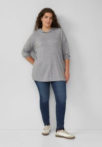 Heathergrijze hoodie met lange mouwen en een V-hals ontwerp, gecombineerd met donkerblauwe jeans en lichtgekleurde sneakers. Eenvoudige, casual stijl.
