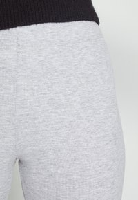 Detailní záběr na světle šedé žebrované legíny v kombinaci s černým pleteným topem, který zdůrazňuje texturu látky a detaily švů.