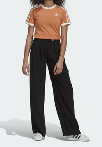 Orange cotton T-shirt with white trim and Adidas logo, paired with black pleated trousers. Footwear: white sneakers with black stripes.