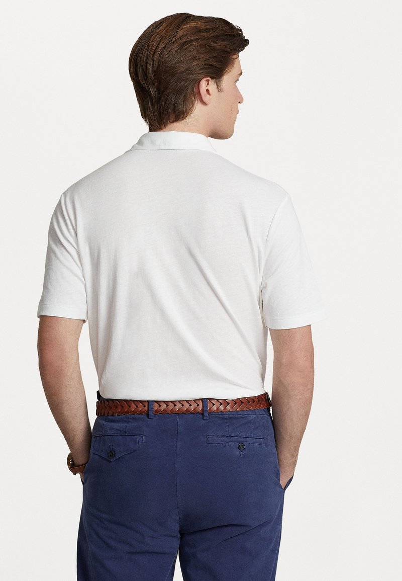 Witte polo met korte mouwen en een klassieke kraag, gecombineerd met marineblauwe broeken en een gevlochten leren riem in bruin.