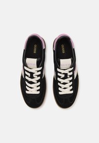 Sorte semskede sneakers med rosa detaljer, hvite skolisser og en beige stripe. Har en logo på tungen og en teksturert gummisåle.