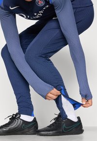Navy athletic long-sleeve top and tapered leggings with ribbed texture. Black shoes with green detailing. White socks visible.