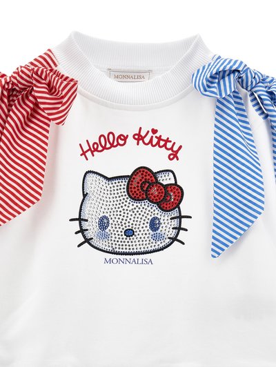 Bela otroška majica z bleščicami v obliki obraza Hello Kitty, rdeče-modri črtasti pentljami na ramenih ter napisom "Monnalisa" spodaj.