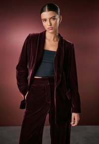 Burgundy velvet blazer with a notched collar and front pocket, paired with matching wide-leg pants and a black cropped top.