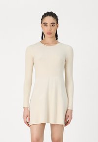 Abito a maniche lunghe in maglia a coste di un beige chiaro. Parte superiore aderente con un orlo svasato. Texture liscia con una leggera lucentezza, scollatura rotonda e design minimalista.