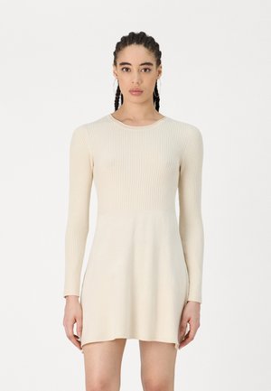 Robe en tricot côtelé à manches longues de couleur beige clair. Haut ajusté avec un ourlet évasé. Texture lisse avec un éclat subtil, décolleté rond et design minimaliste.