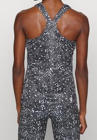 Top sportivo a colletto largo in bianco e nero con motivo, realizzato in tessuto elasticizzato, caratterizzato da una texture leggera e traspirante.
