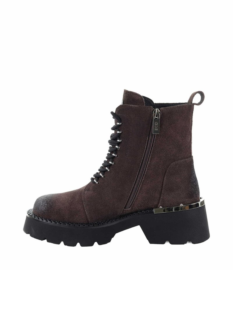 Brązowy zamszowy botek sięgający kostki z czarnymi sznurówkami, bocznym zamkiem błyskawicznym i masywną czarną podeszwą. Posiada metaliczne akcenty i wzmocniony czubek.