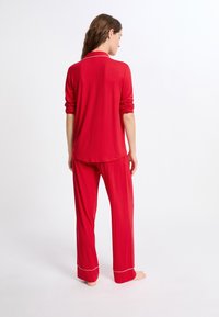 Czerwony zestaw piżamowy składa się z długiego rękawa i pasujących spodni. Miękka, lekka tkanina z kontrastowym obszyciem na mankietach i kołnierzyku.