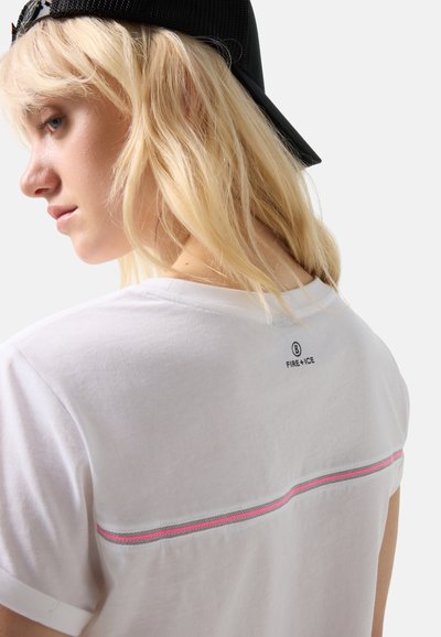 Blonde Frau, die eine schwarze Kappe rückwärts trägt und ein weißes T-Shirt mit einem rosa-grauen Streifen über dem Rücken sowie dem Schriftzug "FIRE+ICE" nahe dem Halsausschnitt trägt.