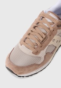 Hellbraune Sneaker mit Suede- und Meshmaterialien, runder Form, Schnürsenkeln, charakteristischem Branding und strukturierten Akzenten nahe der Sohle.