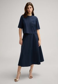 Navyblaues zweiteiliges Kleid mit einem kurzen Oberteil mit kurzen Ärmeln und einer Tasche, kombiniert mit einem langen, fließenden Rock. Glatte Stofftextur.