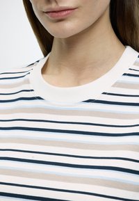 Τοπ με γιακά και οριζόντιες ρίγες σε κρέμ, μπεζ, ανοιχτό μπλε και ναυτικό μπλε. Απαλό βαμβακερό ύφασμα με λείες υφή και εφαρμοστή γραμμή.