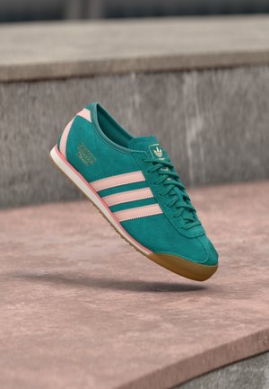 Turkooizen suède sneaker met roze strepen, gestructureerd bovenwerk en gouden logo detail. Lichtbruine rubberen zool, klassiek ontwerp en vetersluiting.