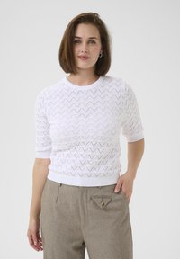 Maglione bianco a maniche corte con un motivo triangolare testurizzato, colletto rotondo e orlo a coste. Abbinato a pantaloni beige chiaro su misura con una tasca a triangolo unica.