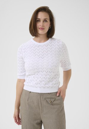 White short-sleeve sweater with a textured triangular pattern, round neckline, and ribbed hem. Paired with light brown tailored trousers featuring a unique triangle pocket.