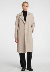 Manteau en laine beige clair avec un col cranté, design à un seul bouton, trois boutons et poches latérales, associé à un col roulé noir et un jean.