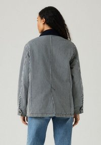 Gestrikte blazer in marineblauw en wit, gemaakt van een gestructureerde stof. Bevat een kraag, knopen en een relaxte pasvorm. Gepaard met lichtblauwe jeans.