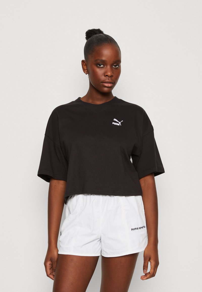 Maglietta nera cropped con scollatura rotonda e maniche corte, caratterizzata da un logo Puma bianco sul petto. Abbinata a pantaloni corti bianchi.