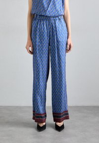 Modre hlače s vzorcem, zasnovane s diamanti, ki imajo rumene poudarke, elastičen pas in maroonske kontrastne manšete. Mehka tkanina.