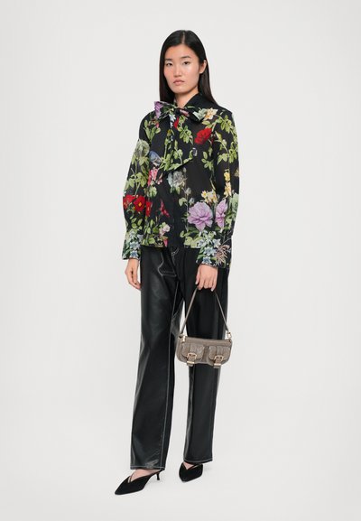 Floral blouse with long sleeves and bow tie, black background, paired with shiny black wide-leg pants, holding a small gray handbag.
