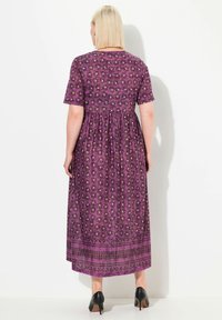 Violetti kukkakuviollinen maksimekko, jossa on lyhyet hihat, kerätty vyötärö ja helmassa tummempi kuviollinen nauha; yhdistetty mustiin kenkiin.